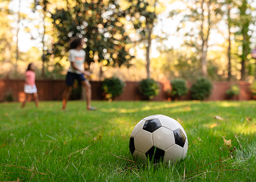 Kids playing outdoors with a soccer ball in the grass.