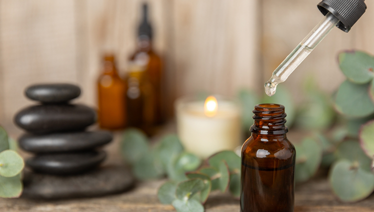 A dropper hanging out an essential oil bottle with a serene spa background.