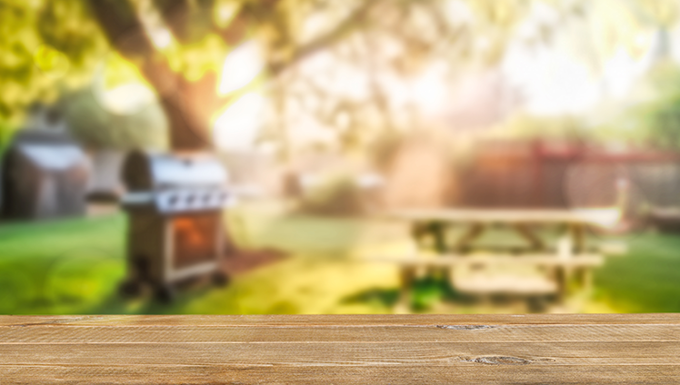 A picture of a picnic table in the foreground with a gas grill and another picnic table in the background.