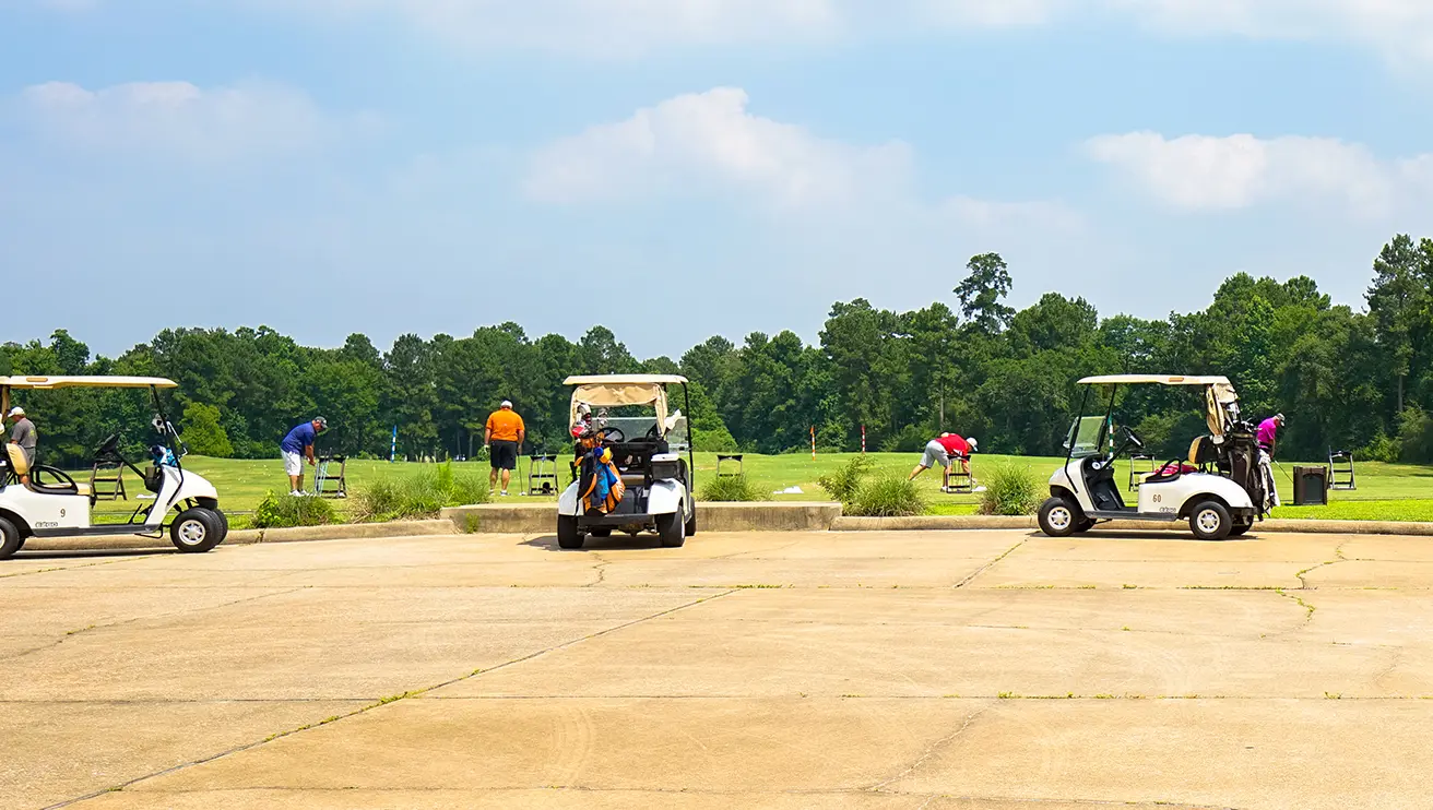 A picture of golf carts in the foreground and golfers at the driving range in the background.