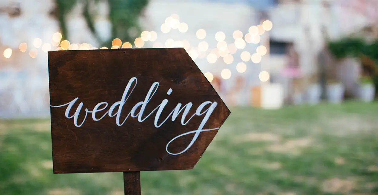 A sign with the word wedding pointing towards a setting for a wedding ceremony.