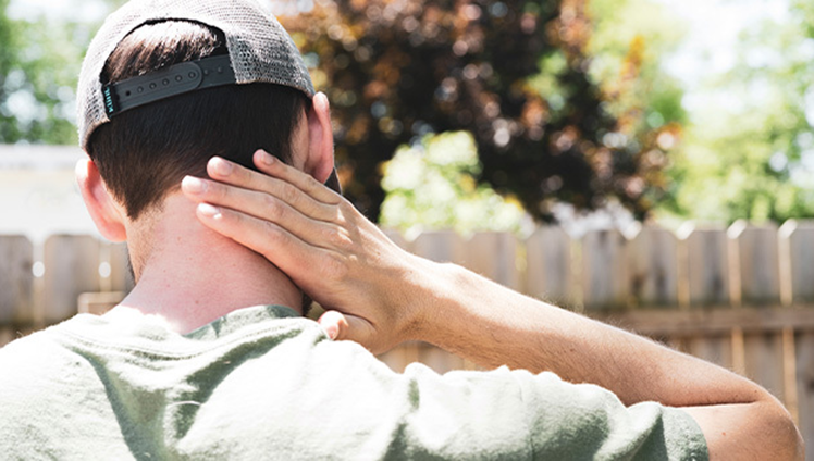 Man wearing a hat is swatting a bug on the back of his neck.