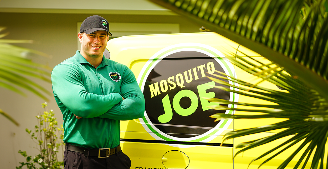 Mosquito Joe professional standing with arms crossed in front of company van's logo.