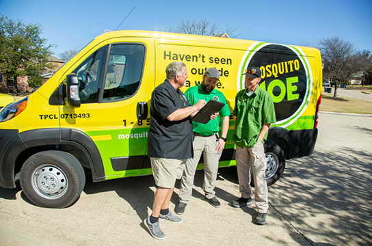 Two Mosquito Joe employees talking with a customer in front of a Mosquito Joe van.