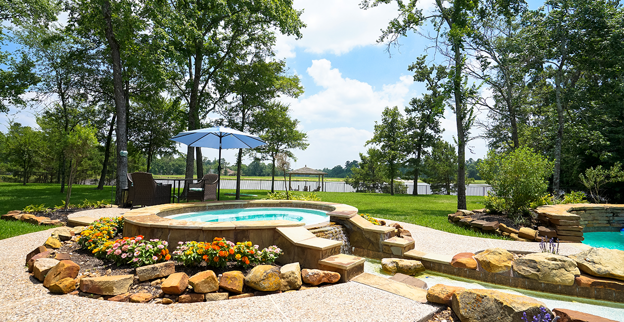 A garden and a pool with a lake in the distance.