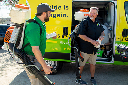 Two Mosquito Joe professionals getting equipment from company van while talking.