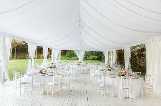 Underneath a white tent with fancy table set ups for an event.