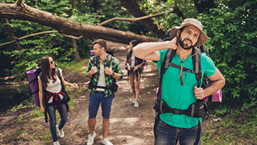 A man on a hike with friends swatting at a mosquito on their  neck.