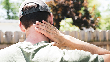 Man wearing a hat swatting bugs from his neck.