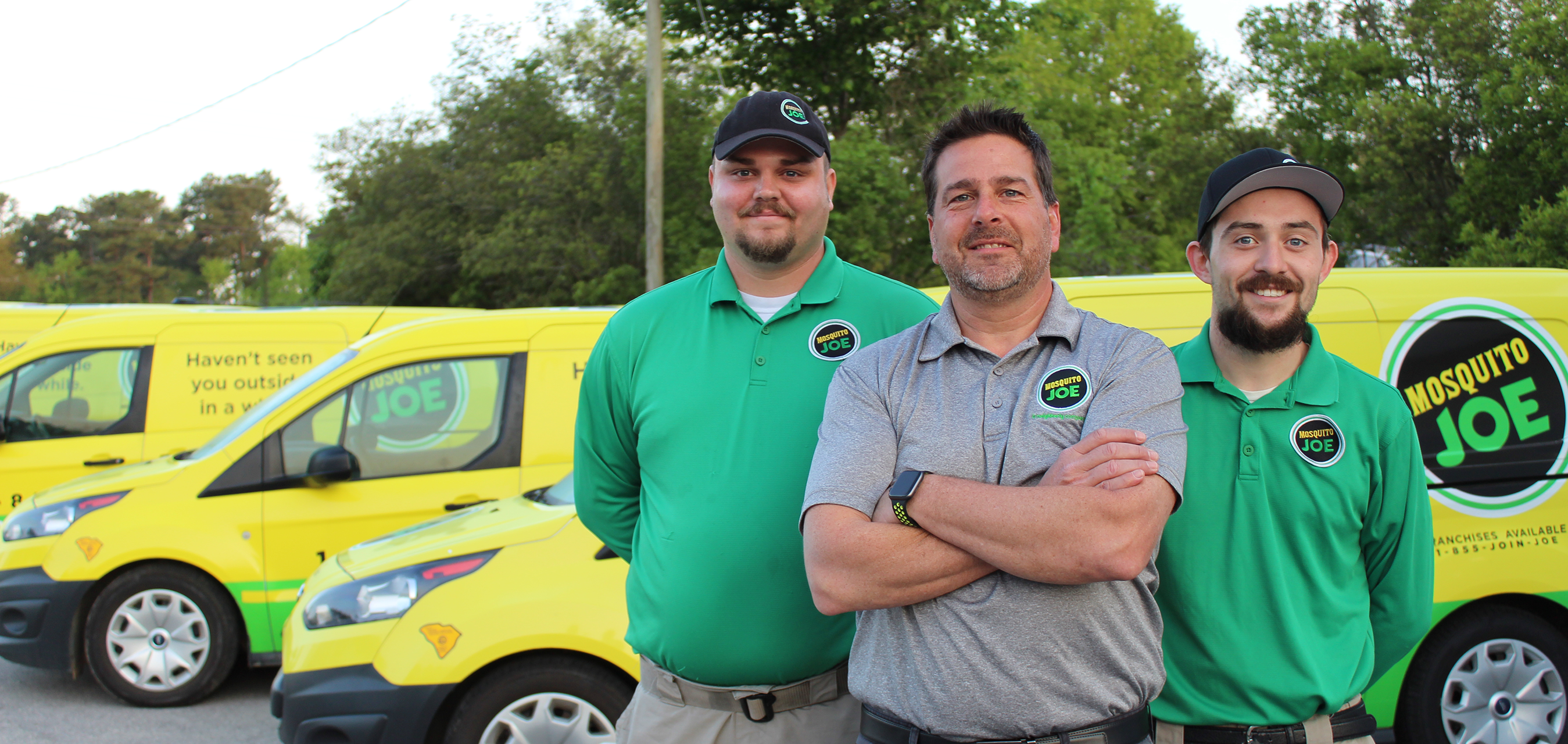 Three Mosquito Joe professionals posing in front of company vans.