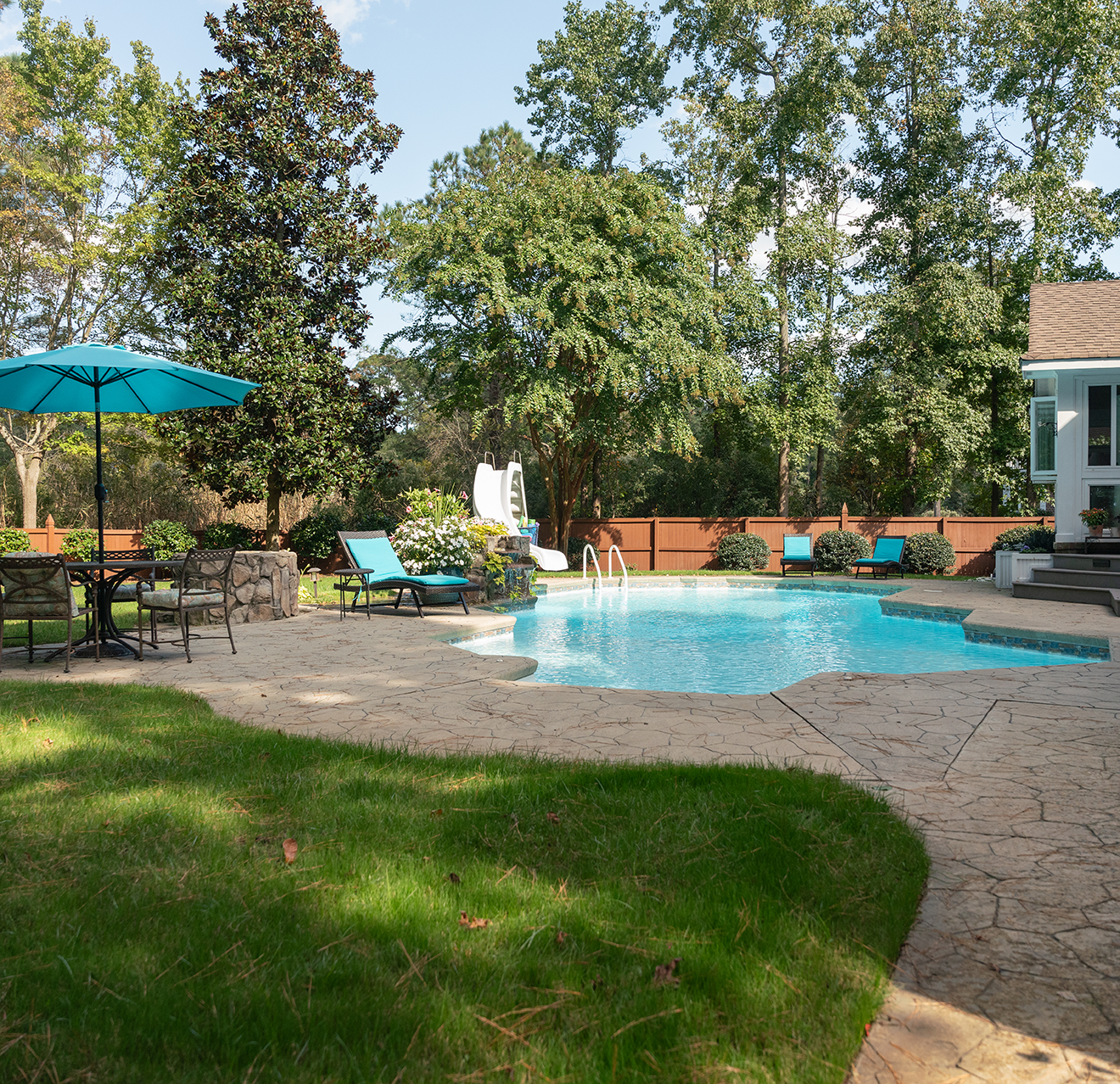 Backyard pool with a water slide and a picnic table.