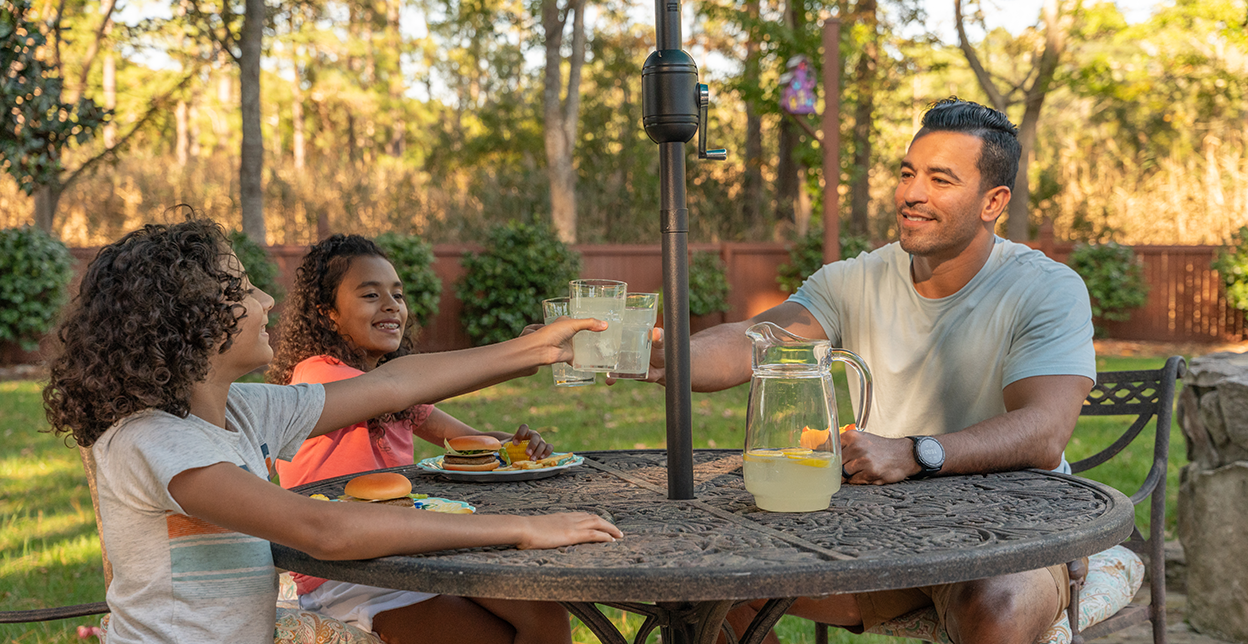 Dad and kids outside doing a cheers with glasses of lemonade.