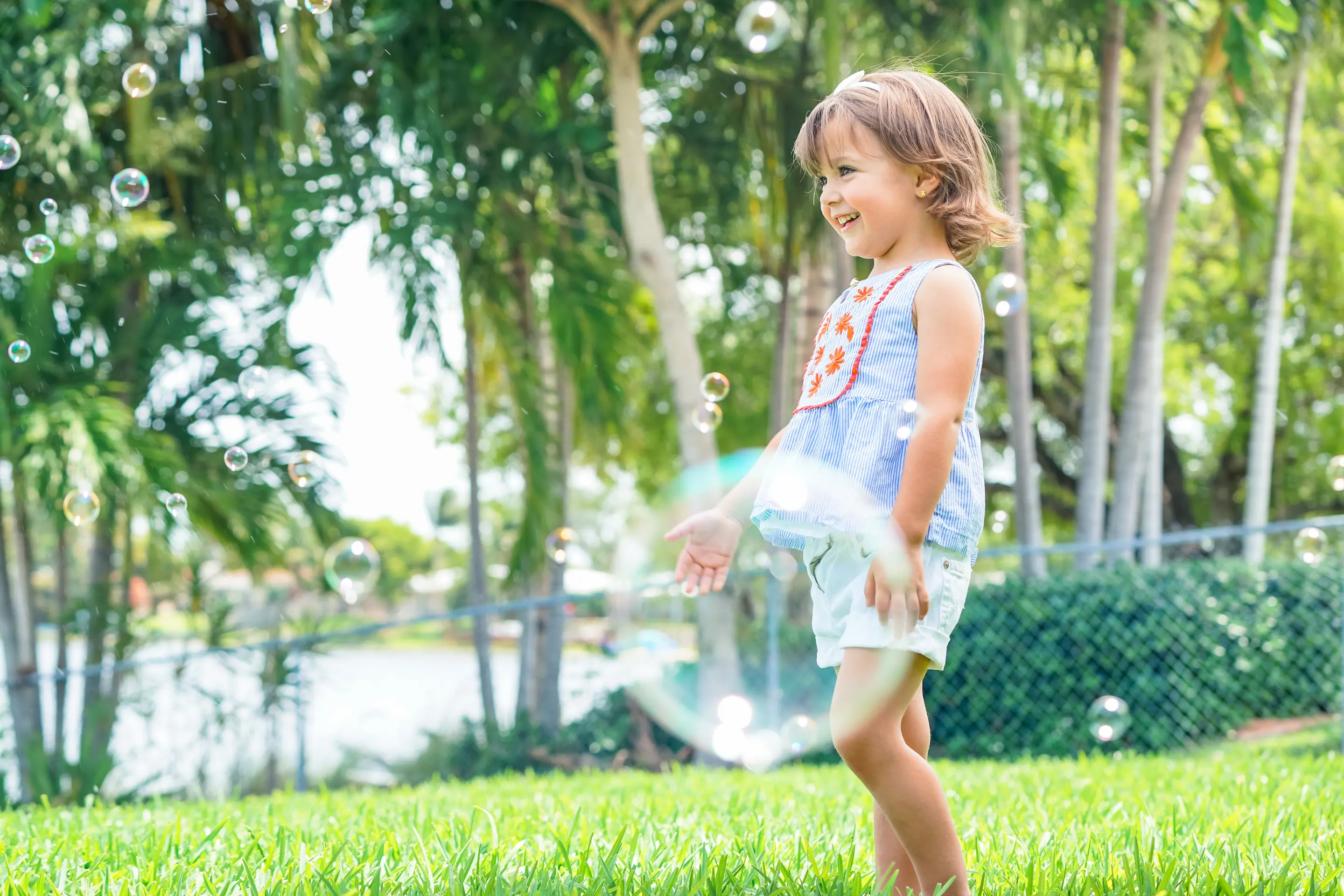 Little girl blowing bubbles outside in yard.