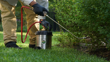 A man uses a sprayer to treat weeds in the grass.