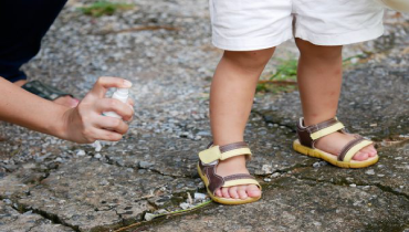 Parent spraying bug repellent on toddler's leg and feet outside.