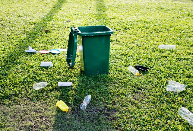 Empty plastic bottles laying next an open trash can.