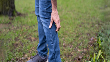 Man outside scratching his leg over jeans from mosquito bites.