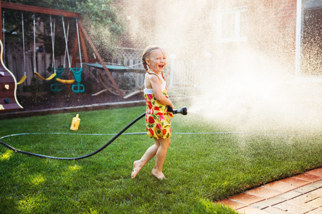 Child playing with water outside at sunset.