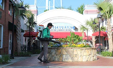 Mosquito Joe technician wearing a long-sleeved green shirt and khaki pants sprays barrier treatments to protect commercial properties.