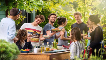 Group of young people having fun outdoors talking while others serve food during a BBQ.