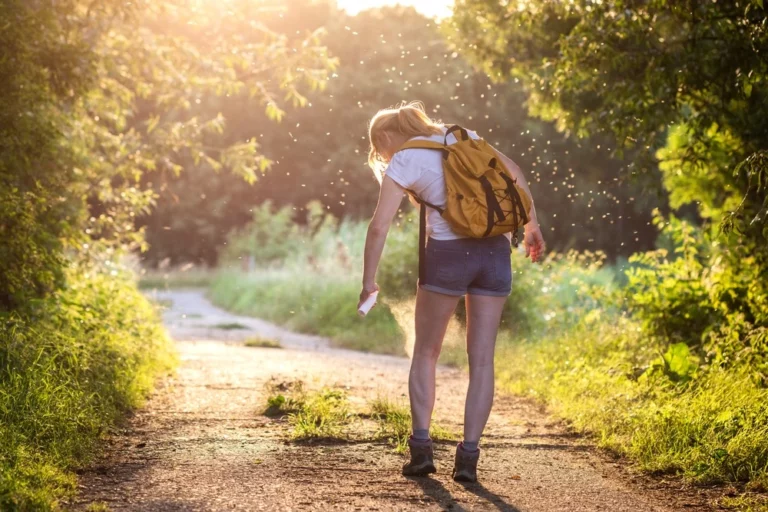 Woman hiker spraying bug spray while walking down trail.