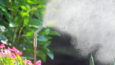 A garden misting system spraying among plants with vibrant flowers in the background.