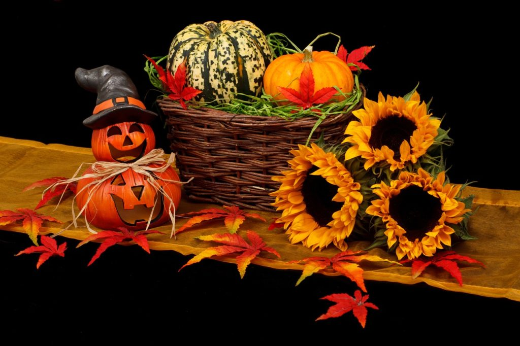 Halloween decor with carved pumpkin, sunflowers, and autumn leaves on black background.