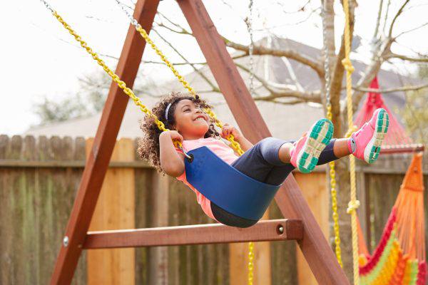  A young girl swings on a swing in a sunny backyard.