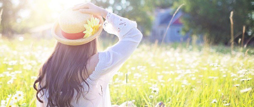 A woman wearing a hat sits peacefully in a lush green field.