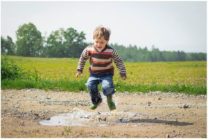 Little kid jumping in puddle of water in a field.