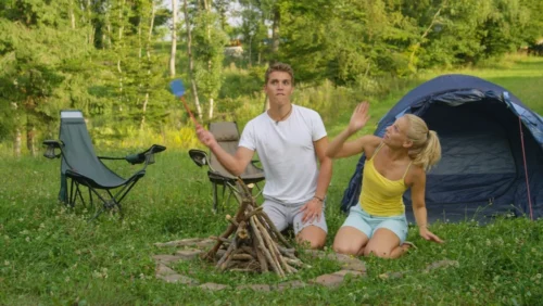 Young couple swatting mosquitos away outside tent.