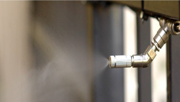 A close-up of a metal faucet with water spraying out, against a blurred background.