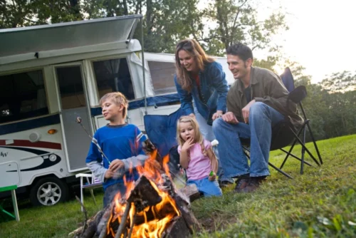 Family sitting around campfire with smores outside of RV.