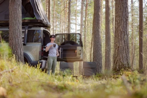 Woman standing drinking coffee outside of RV while camping in the woods.