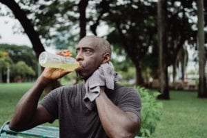 Man drinking from a bottle with a towel over his shoulder.