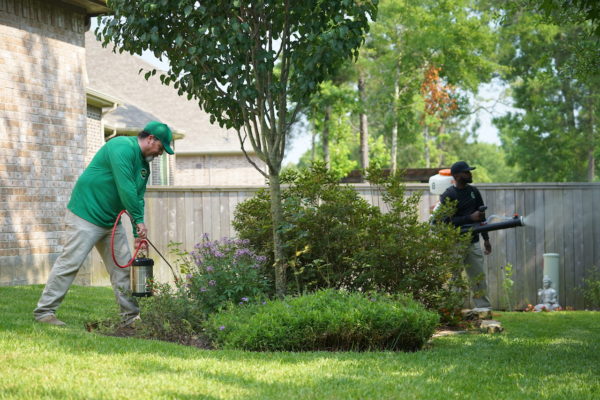 Two men in green attire are actively working in a yard.