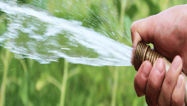 Man holding tip of hose with thumb and spraying water.